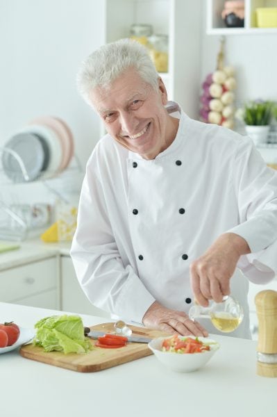 Portrait Of Elderly Male Chef Pouring Oil Into Salad